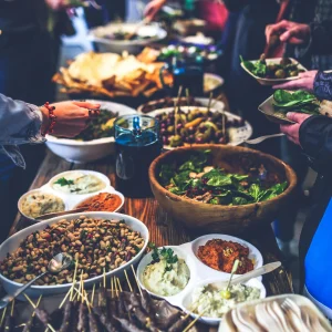 Buffet convivial présentant divers plats méditerranéens comme du houmous, des olives, des brochettes de viande et des salades composées.