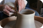 Gros plan sur les mains d'un artisan potier façonnant avec précision le rebord d'un vase en argile blanche sur un tour de potier.