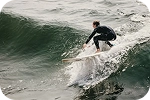 Un surfeur en combinaison noire en pleine action sur le flanc d'une vague écumante dans l'océan.